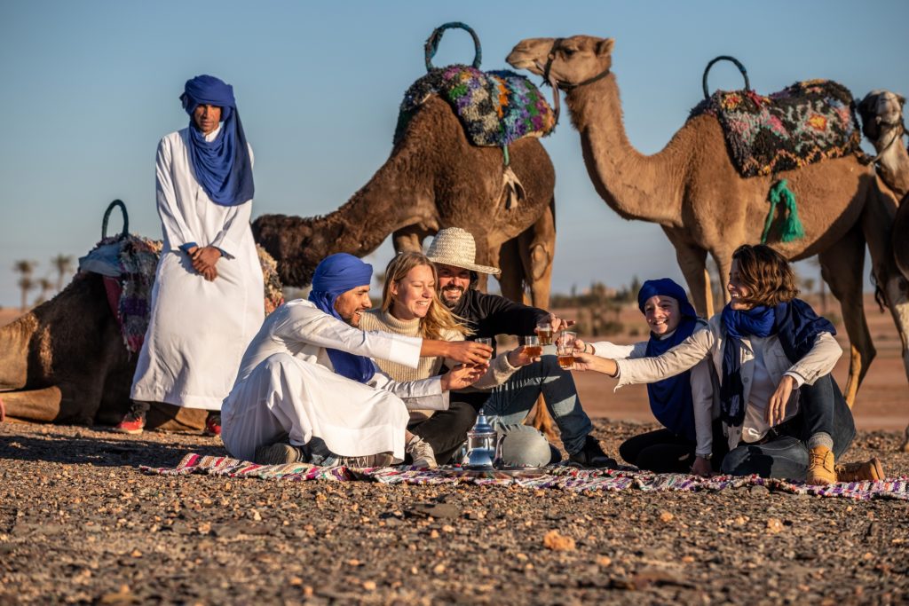 Voyageurs partageant un thé à la menthe avec les guides à côté des dromadaires dans le désert d'Agafay