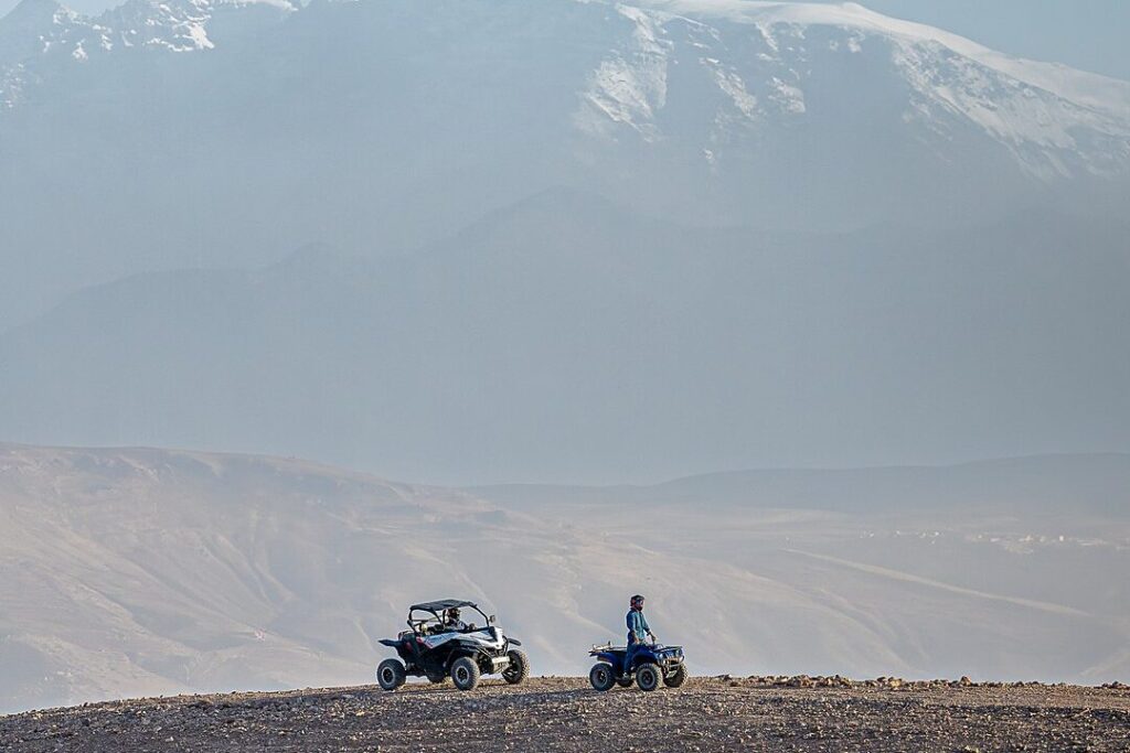 Un buggy et un quad sur une crête du désert d'Agafay, avec les sommets enneigés du Haut Atlas en arrière-plan